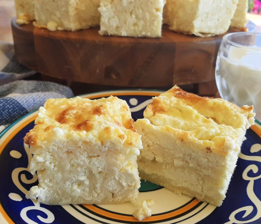 Close-up shot of ricotta and fillo bake cut into squares, served with small glass of milk