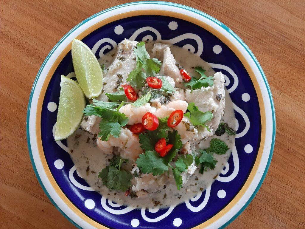 Overhead photo of this 20-minute Thai fish curry, served in a decorative bowl. with suggested garnishes like chilli, lime wedges, and fresh herbs
