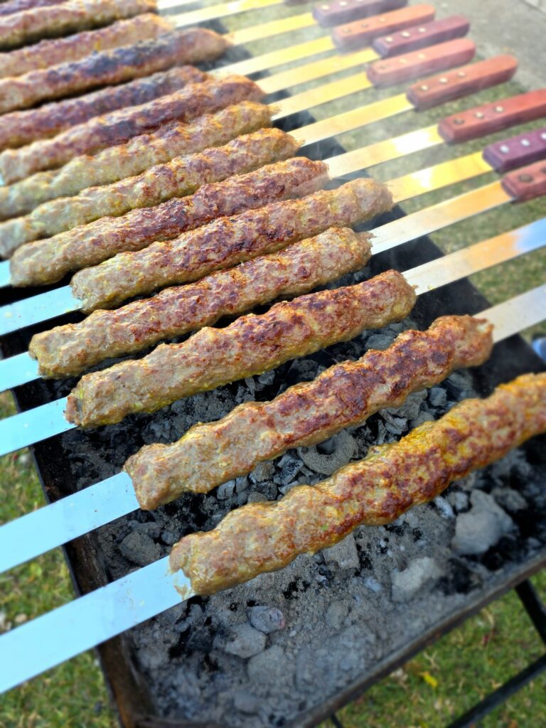 Close-up photo of Persian Kebabs (Kabob Koobideh) cooking on a charcoal barbecue, showing how low the heat needs to be to not burn the meat
