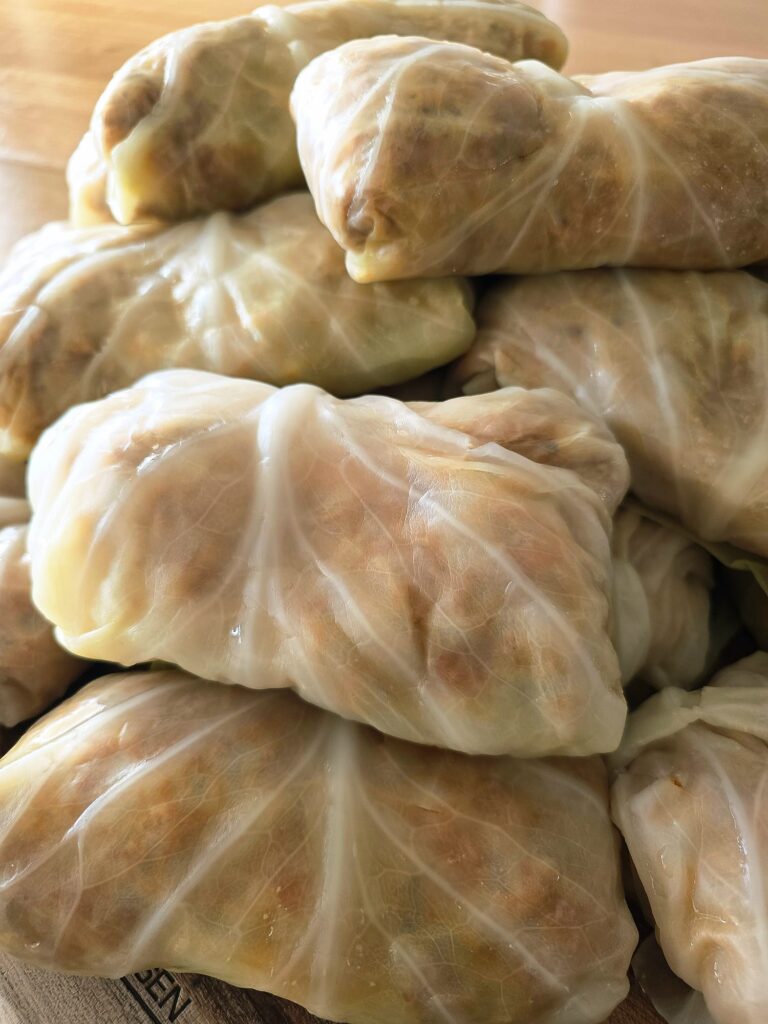 Close-up photo of a stack of rolled-up Balkan Stuffed Cabbage Leaves (Sarma) on a wooden board
