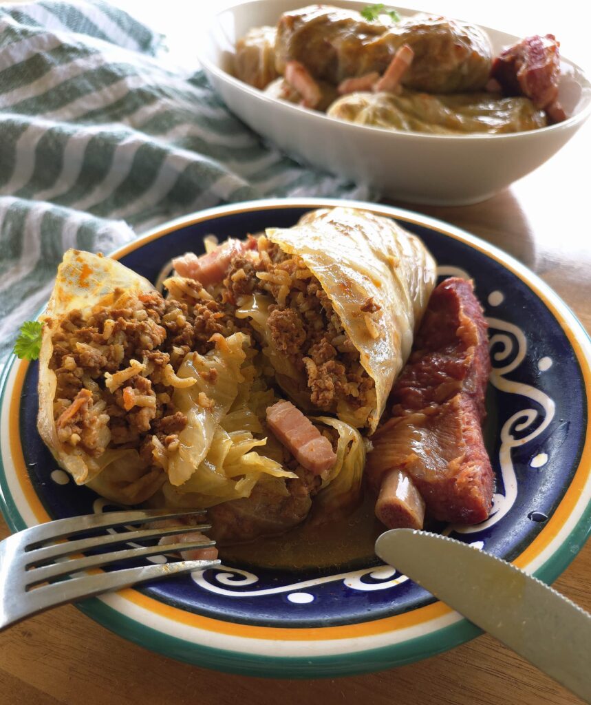 Close-up photo of one of the Balkan Stuffed Cabbage Leaves (Sarma) cut open, showing the pork mince filling inside, served in a decorative blue and white bowl