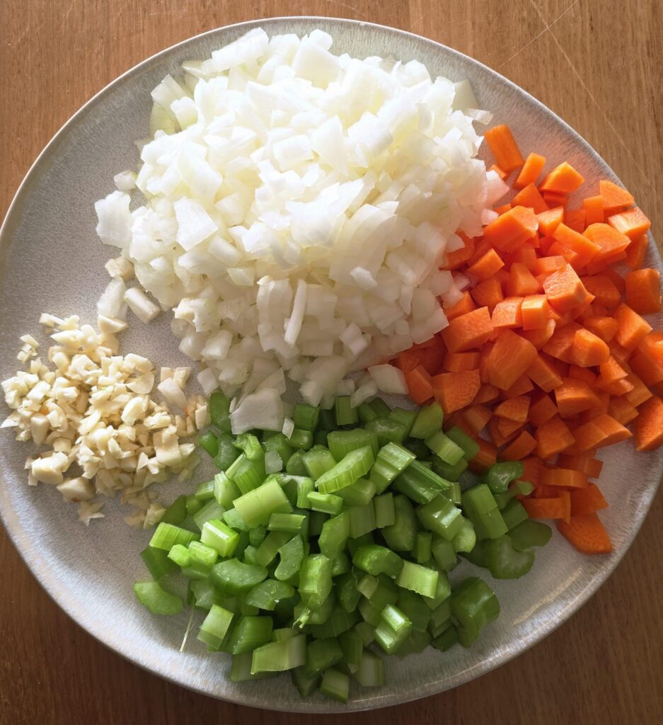Overhead photo of the mirepoix for this ham and pea soup - a white plate showing chopping onions, carrot, celery and garlic