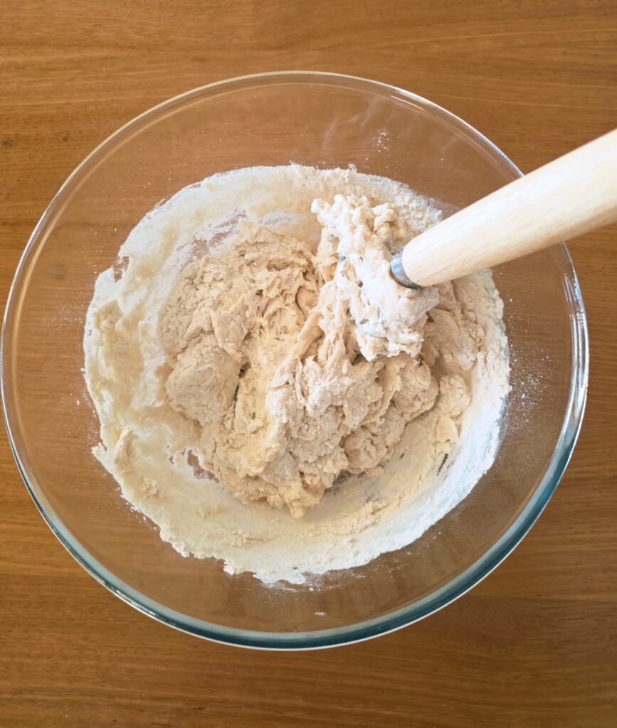 Photo of salt, flour, water, and starter being mixed in a glass bowl