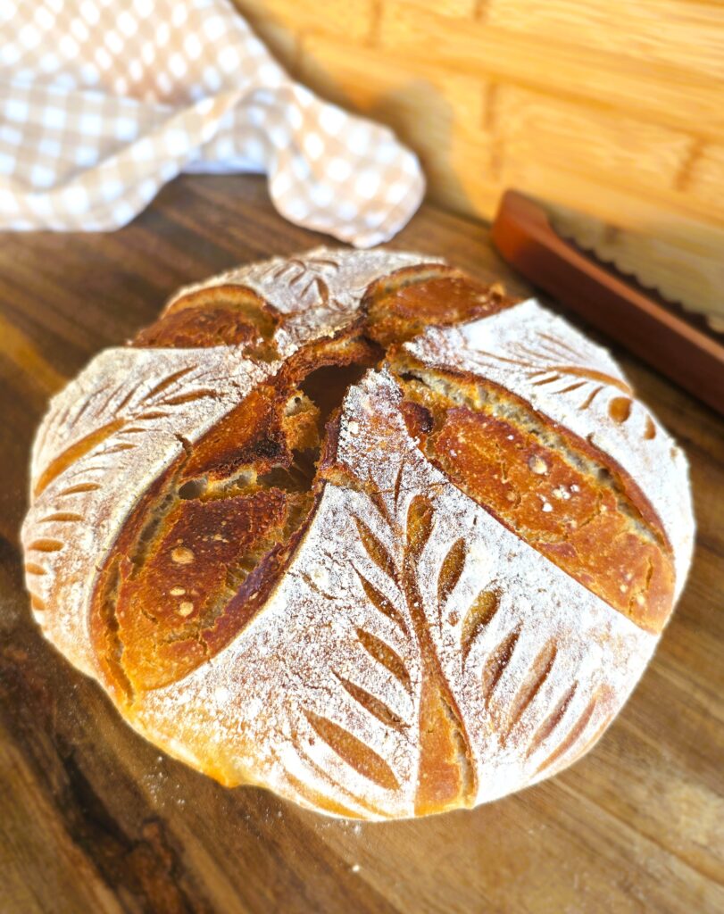 A perfectly baked loaf of sourdough bread with decorative scoring pattern
