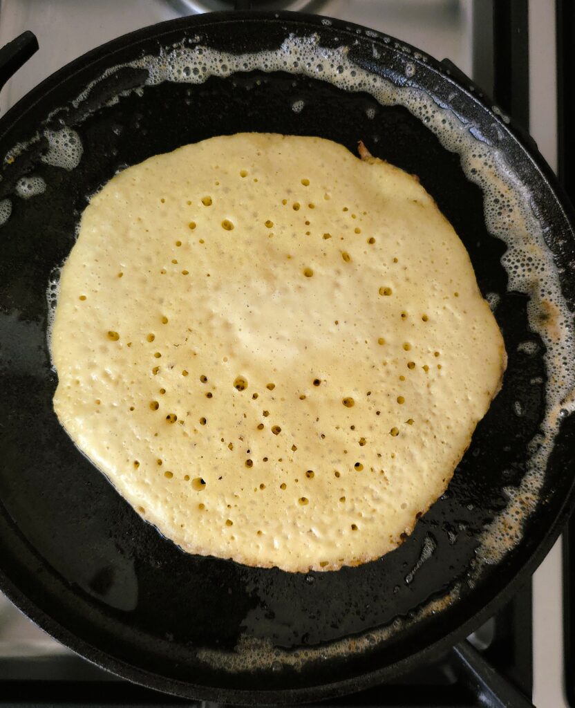 Cooking sourdough discard pancake in cast iron skillet in butter until bubbles appear